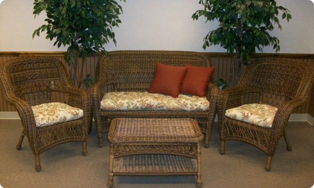 Brown wicker furniture with red accent pillows and a printed seat cushion.