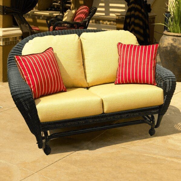 An outdoor wicker loveseat with yellow cushions and red striped throw pillows.
