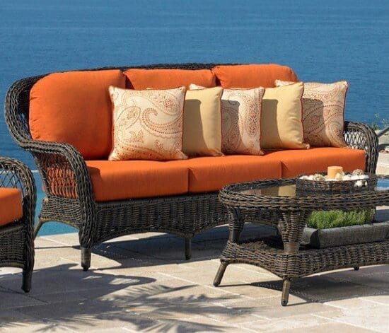 A dark brown wicker sofa with dark orange cushions and yellow accent pillows.